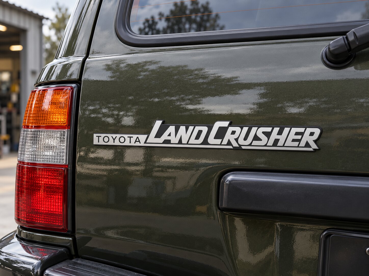 Silver and black Land Crusher emblem mounted on an olive Land Cruiser tailgate